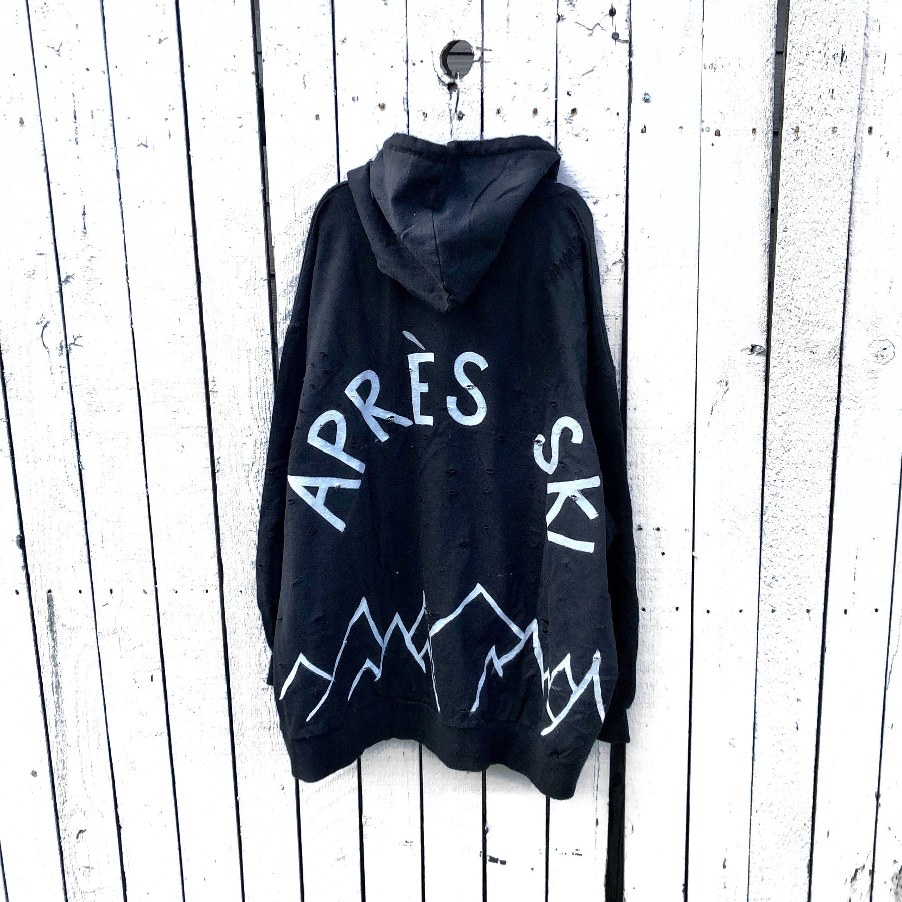 The perfect oversized black distressed hoodie. APRES SKI painted on back in semi circle, with mountain outline along bottom. Signed @wrenandglory