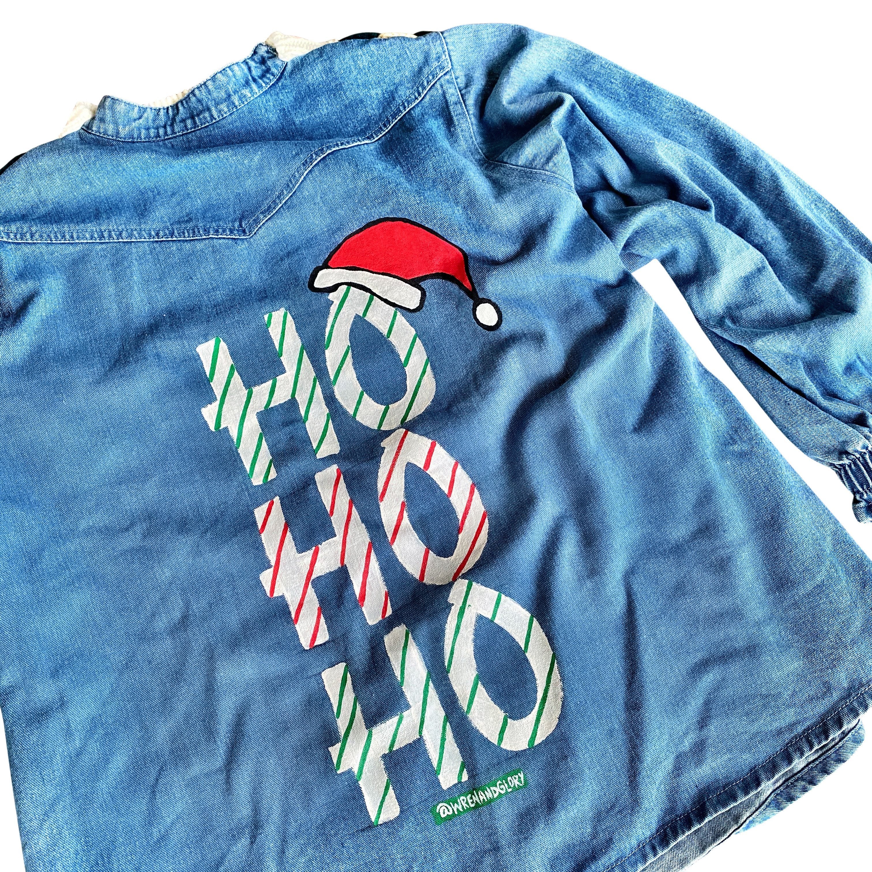 Knit sweater, with denim shirt on back. HO HO HO painted in white, green and red on back with small Santa hat. Signed @wrenandglory.