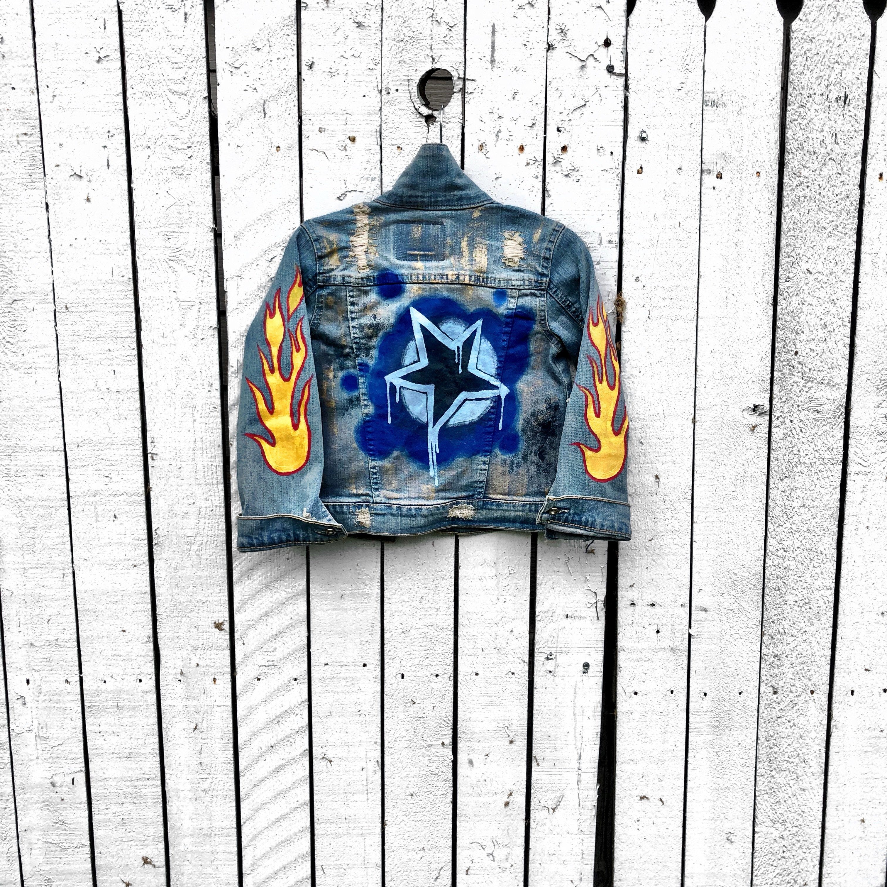 Blue denim jacket. Hand painted design, with stars, flames, and metallics. Childs name available on front, left corner. Each jacket wrapped in a silk wrap bracelet with a child’s charm. Each piece signed @wrenandglory.