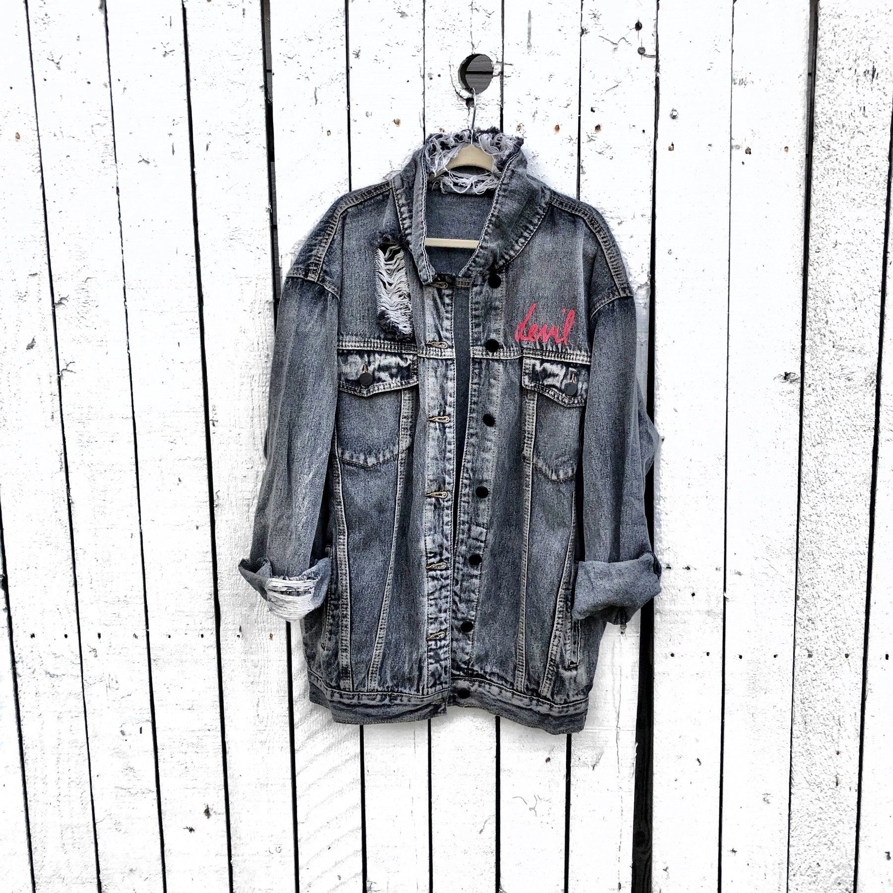 Faded black denim. Red devil wings, horns and tail painted on back, with 'devil' painted in script on front upper corner. Assorted 1 inch pins on front upper side. Signed @wrenandglory.