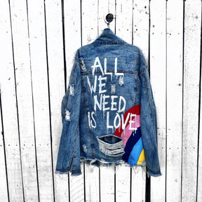 Medium blue denim wash. Large rainbow, spreading across the back to the front, with 'All We Need Is Love' painted in white with a dripping effect. Signed @wrenandglory.