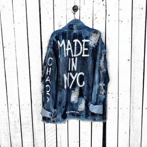 Medium blue denim wash. Black base all over, with 'MADE IN NYC' painted on back in white. CHAOS painted down the arm in white. Assorted 1" pins on bottom left, bottom pocket area. Signed @wrenandglory.