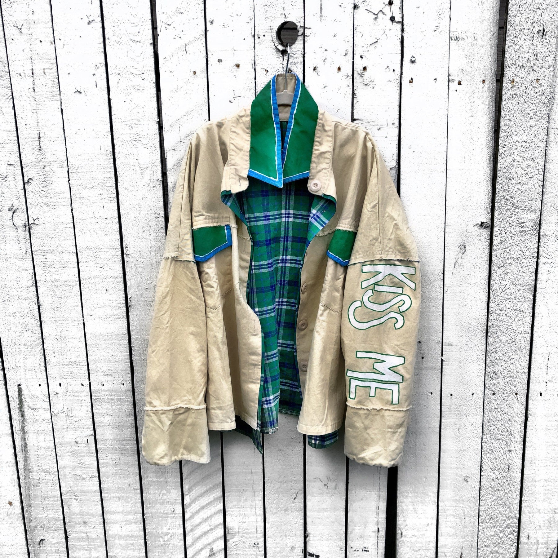 Khaki colored jacket, with green flannel print inside. Large green clover painted on back, with KISS ME down the arm in green and white. Signed @wrenandglory.