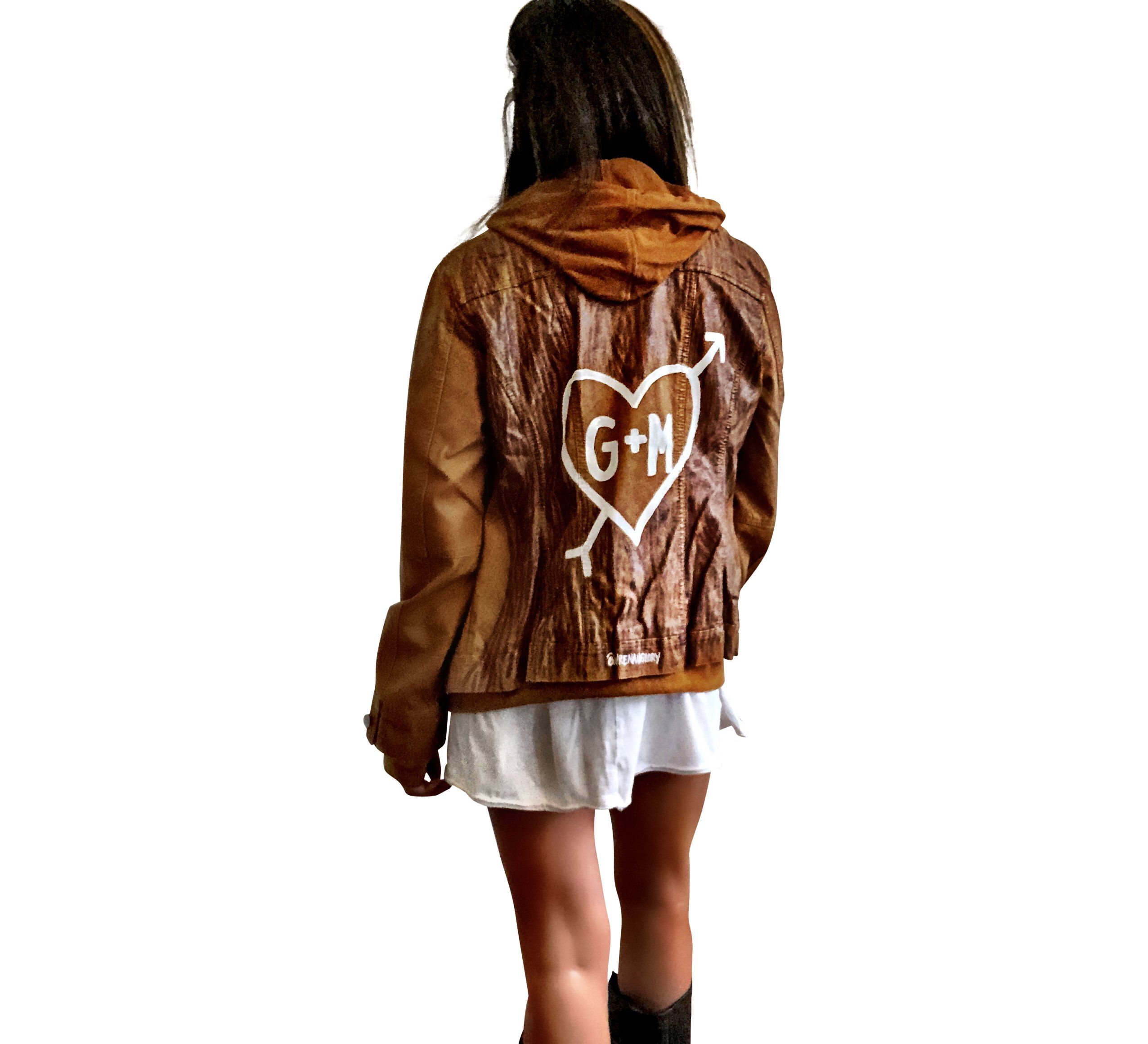 Light brown, faux leather jacket with tan sweatshirt lining the inside, with good and thumbholes at sleeves. Tree trunk painted across entire back in dark brown, with heart carved out and ' ___ + ___' painted inside. Please specify names above. Signed @wrenandglory.