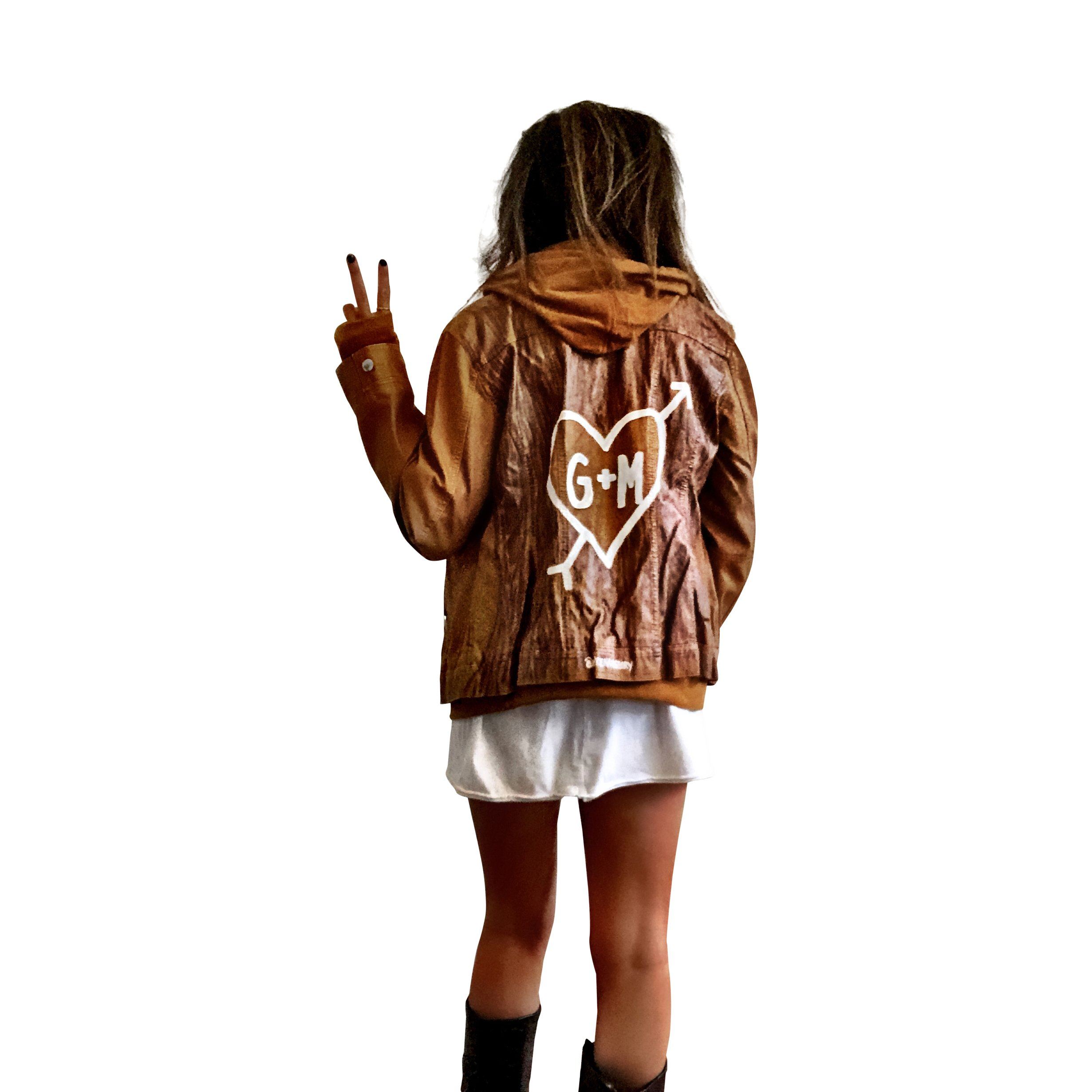 Light brown, faux leather jacket with tan sweatshirt lining the inside, with good and thumbholes at sleeves. Tree trunk painted across entire back in dark brown, with heart carved out and ' ___ + ___' painted inside. Please specify names above. Signed @wrenandglory.