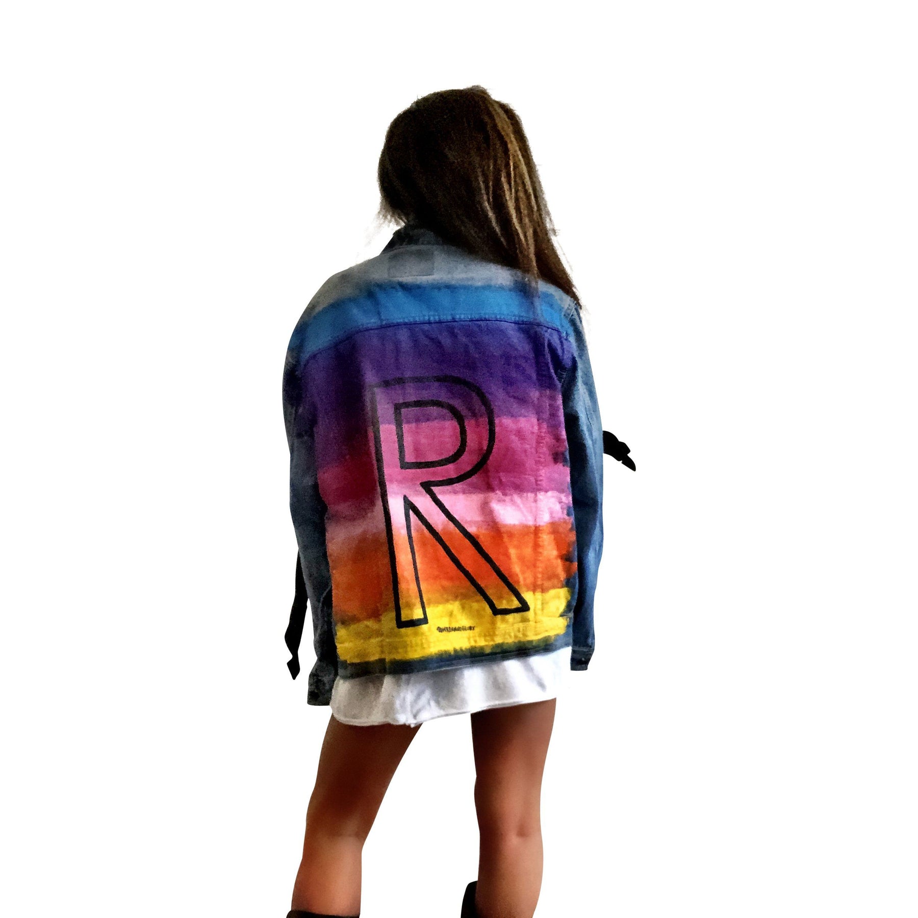 Dark blue denim wash, with velvert ribbon threaded through arms and front, lower left side. Ombre of colored striped on back, with large black initial painted in open block font over the colors. 'BE THE MAGIC' painted on color in black. Please specify initial above. Signed @wrenandglory.