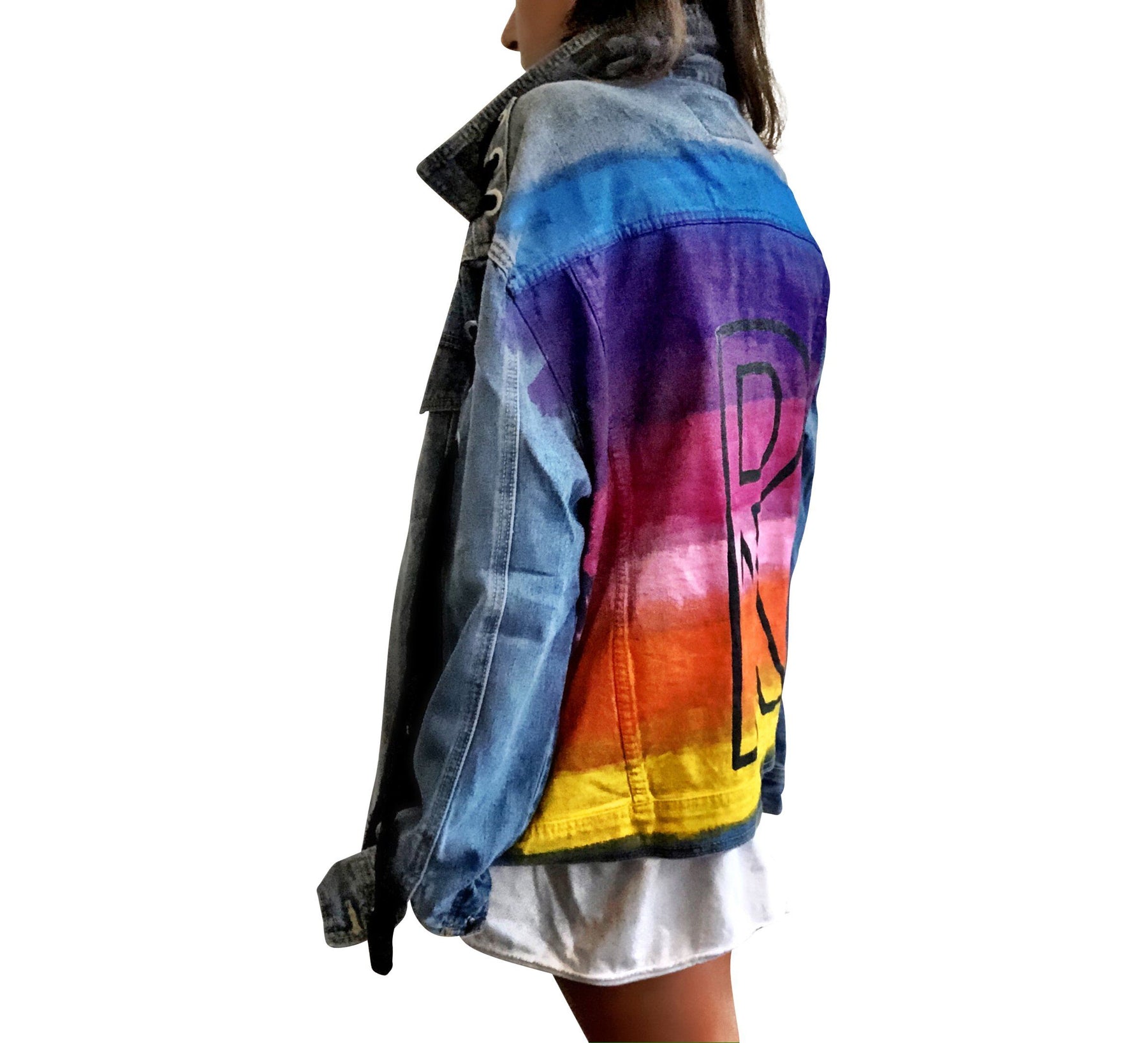 Dark blue denim wash, with velvert ribbon threaded through arms and front, lower left side. Ombre of colored striped on back, with large black initial painted in open block font over the colors. 'BE THE MAGIC' painted on color in black. Please specify initial above. Signed @wrenandglory.