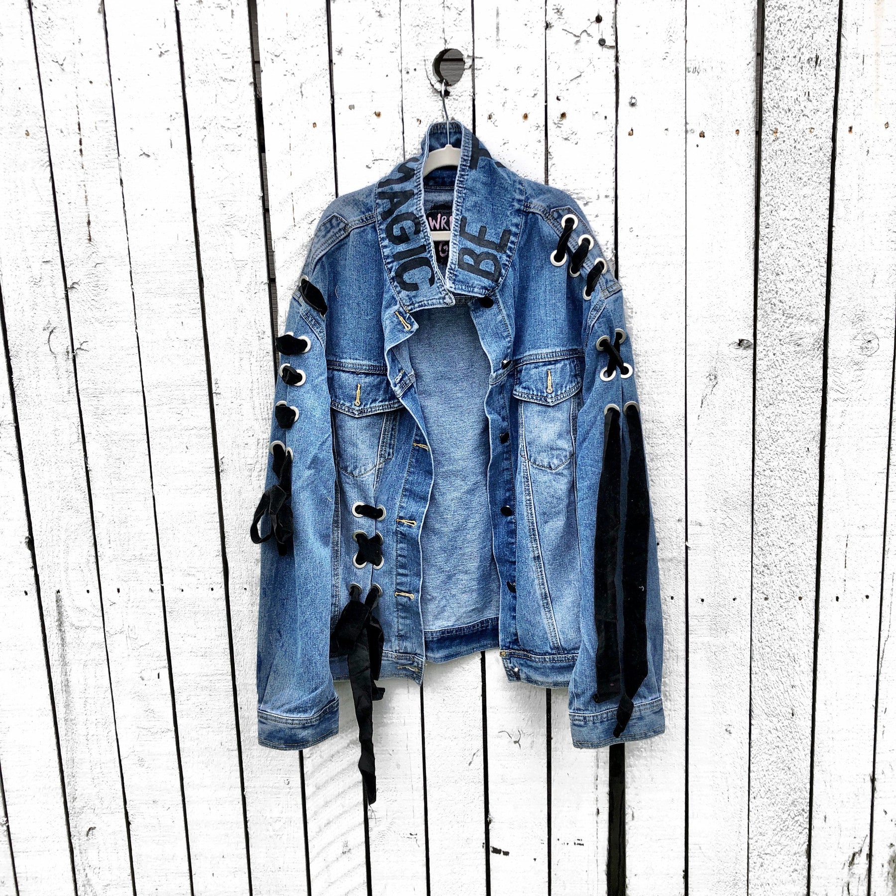 Dark blue denim wash, with velvert ribbon threaded through arms and front, lower left side. Ombre of colored striped on back, with large black initial painted in open block font over the colors. 'BE THE MAGIC' painted on color in black. Please specify initial above. Signed @wrenandglory.