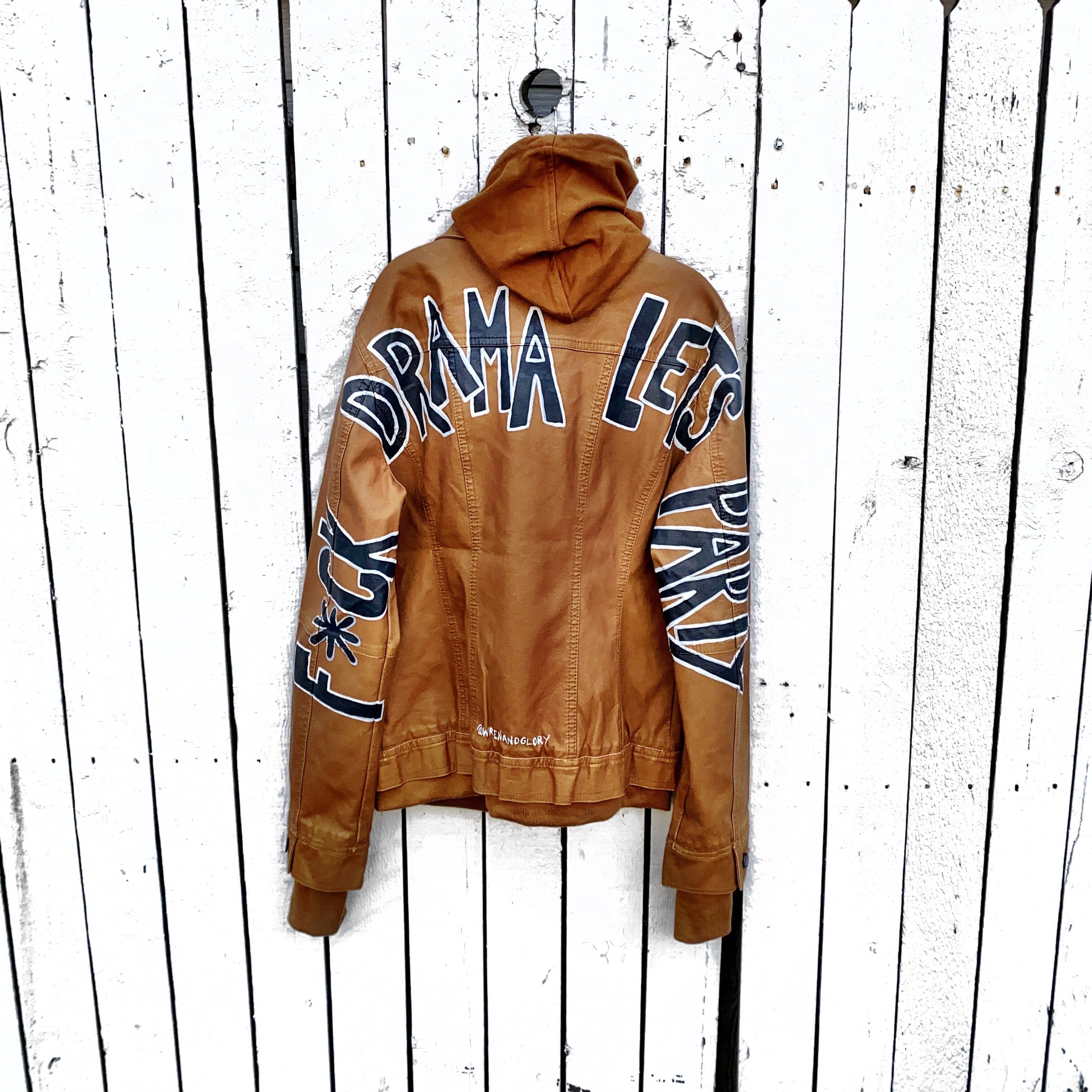 Tan, faux leather jacket with Brown hooded sweatshirt lining the inside and thumbholes at sleeves. 'F*CK DRAMA LET'S PARTY' painted along back of sleeves and upper back of jacket, in black, with white outline. Signed @wrenandglory.