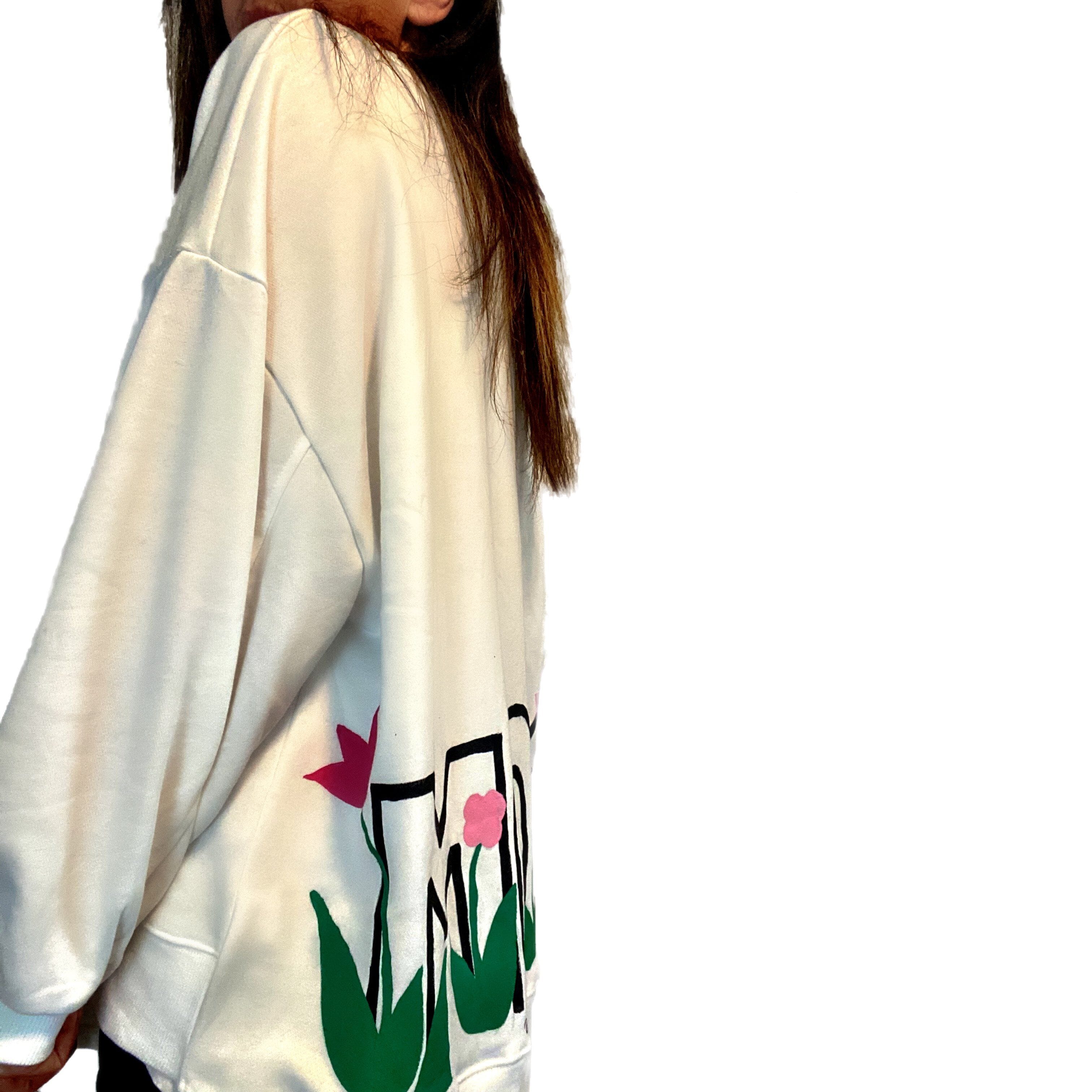 Oversized white sweatshirt. 'MOM' painted in on back, coming up from bottom hem, with flower pattern painted throughout letters. Customized upper back with names of children, grandchildren, husband, etc. Up to 8 names able to be painted. Small red embroidered heart on each lower sleeve. Signed @wrenandglory.