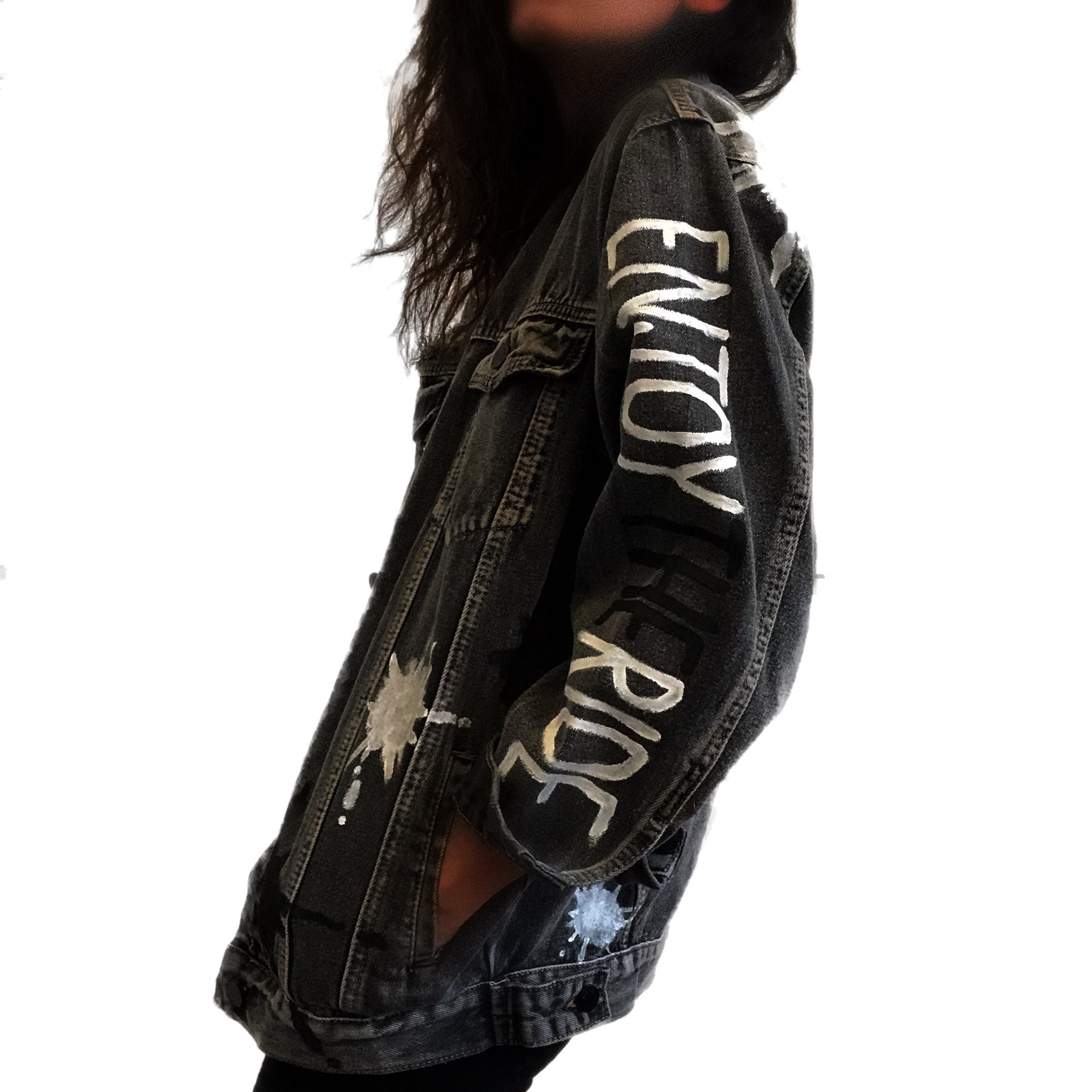 Faded black denim wash. Large white initial on back, with painted white and black 'splatters' 'Enjoy The Ride' painted in black and white down the arm. Signed @wrenandglory.