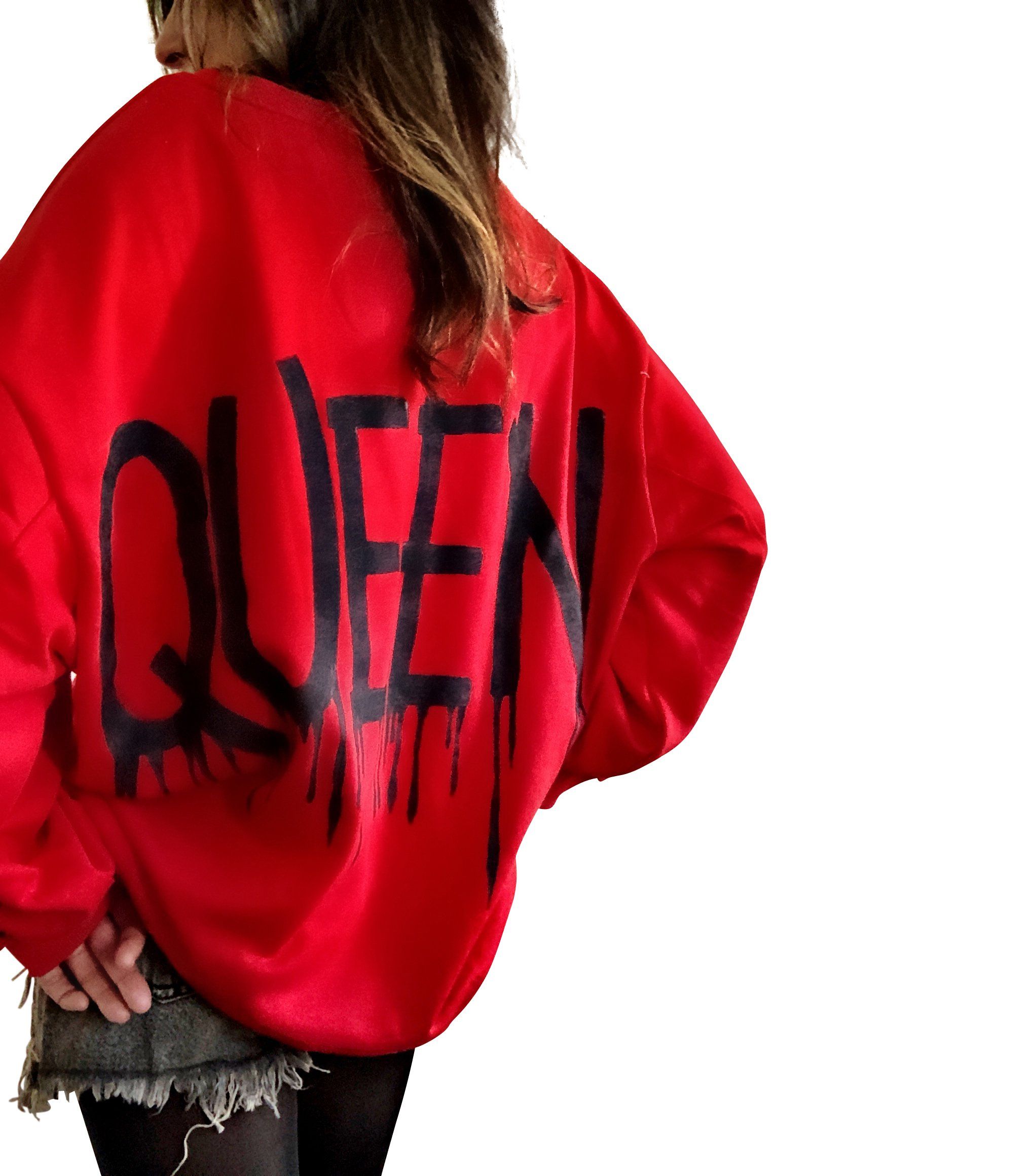 A person wearing an oversized red sweatshirt with 'QUEEN' painted in black on the back and a black crown painted on the front, upper left side.