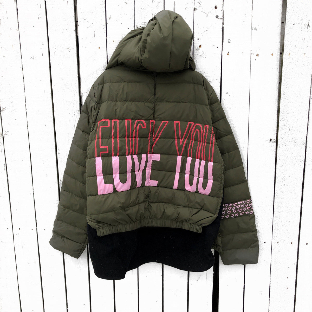 Perfect army green puffer jacket. On back, painted 'LOVE/FCK YOU' in pink and red. Bottom on left sleeve painted with pink hearts all around. Signed @wrenandglory.