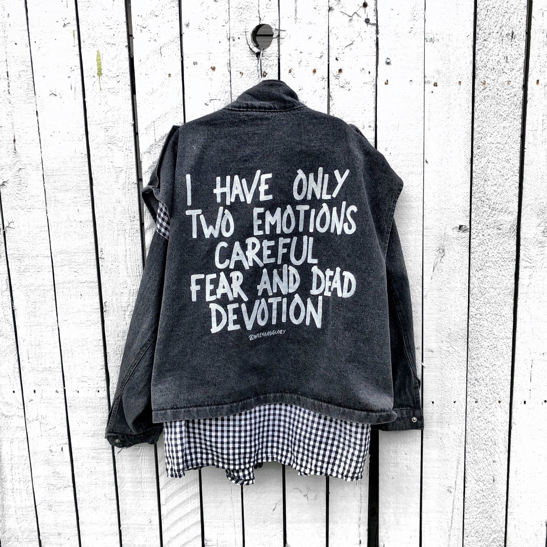 Light black denim, with black and white checkered flannel insert. 'I HAVE ONLY TWO EMOTIONS, CAREFUL FEAR AND DEAD DEVOTION' painted in white on back. ''I CANT GET THE BALANCE RIGHT' painted in white, in small, on front. Signed @wrenandglory.