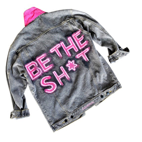 Faded black denim. BE THE SH*T logo painted on back in neon effect in bright pink. Collar and front pockets painted white. Signed @wrenandglory.