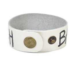 Hand made leather bracelet, hand painted with Bad B*tch and crossbones.  White leather, black paint. Signed W+G