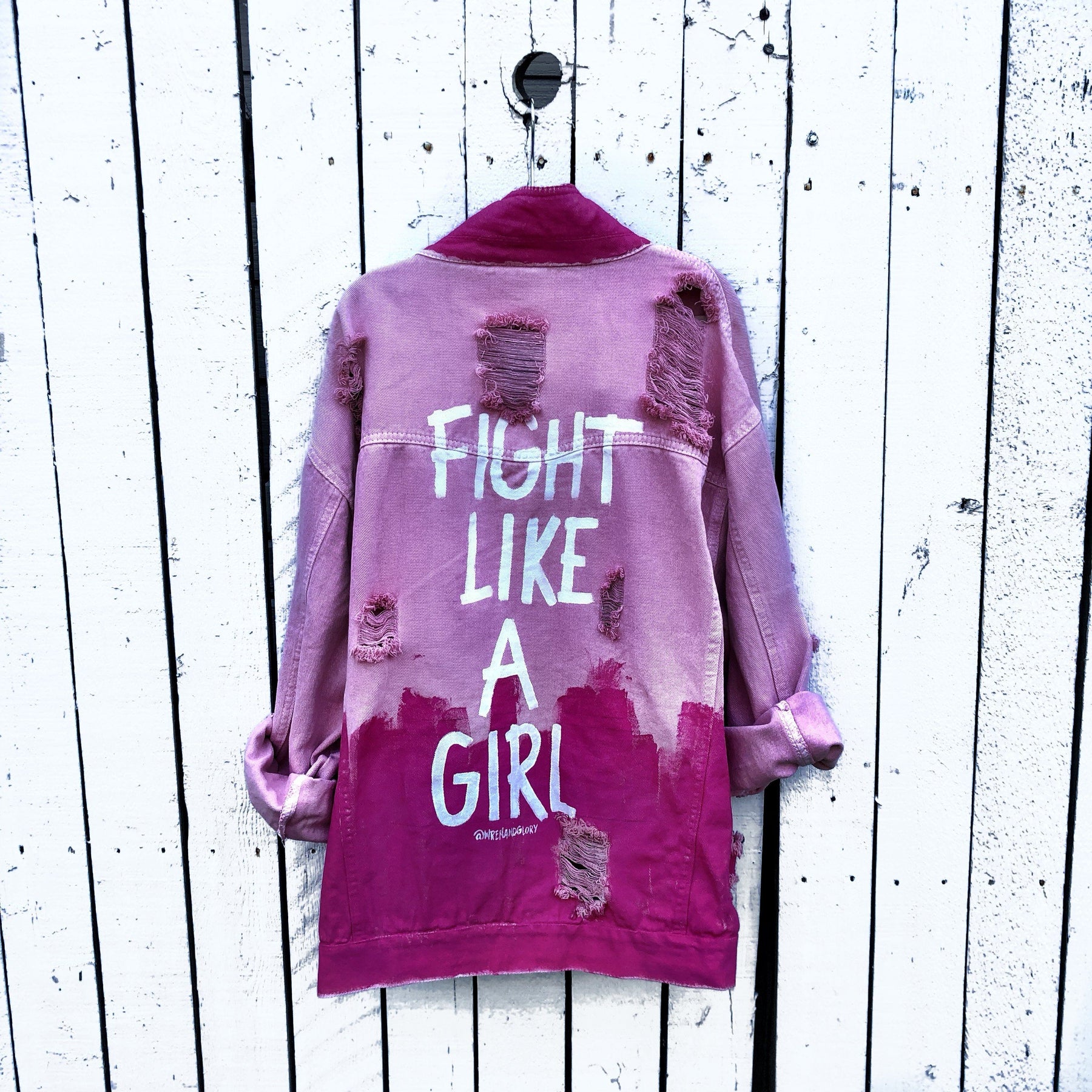 Pink /blush colored denim. Hot pink painted along the bottom half of the jacket, with FIGHT LIKE A GIRL painted in white on back. Small Breast Cancer Awareness ribbon painted on front upper pocket. Signed @wrenandglory.