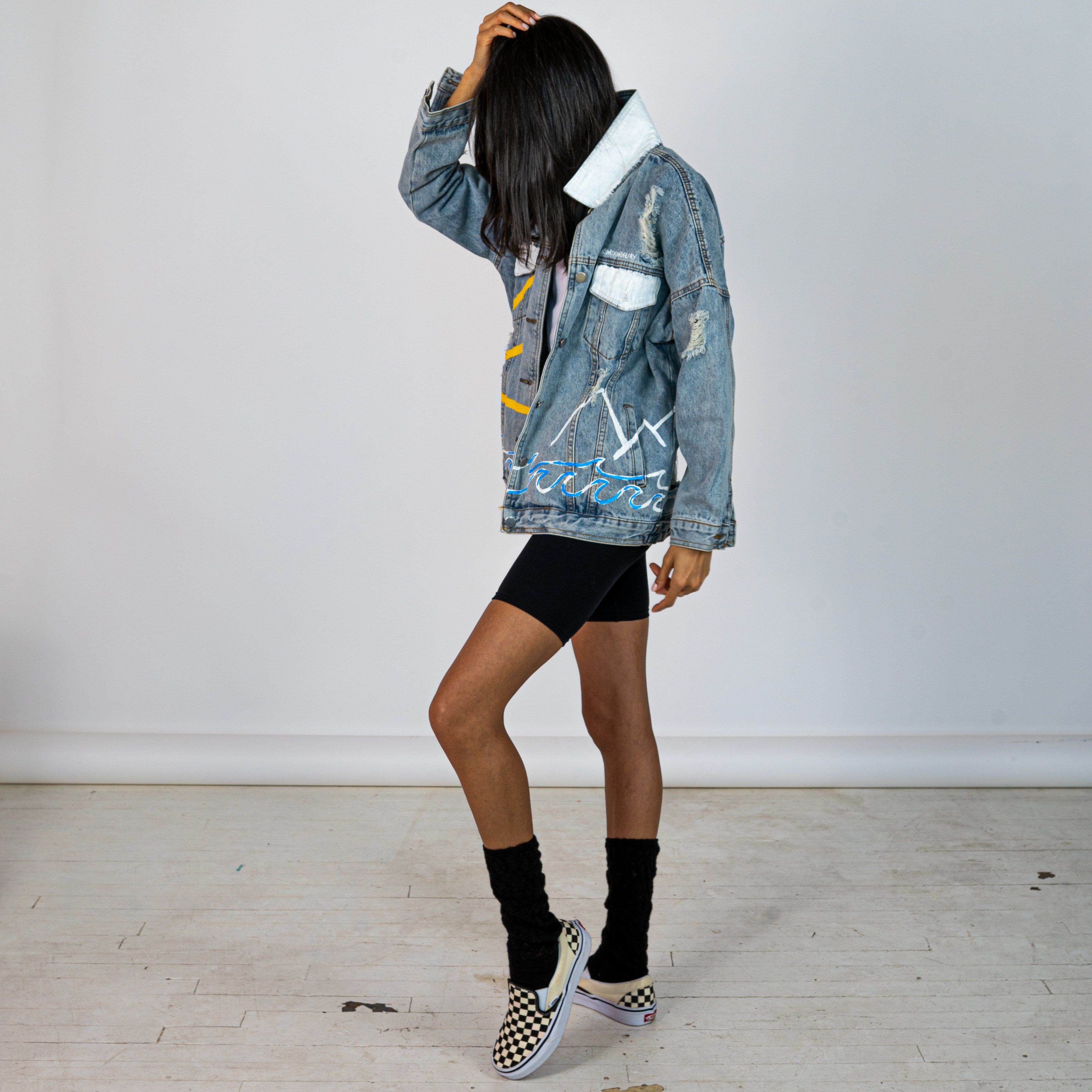 Lighter blue denim wash. Outline of mountain range, ocean waves, and sun setting surrounding entire jacket. Collar and front pockets painted white. Signed @wrenandglory.