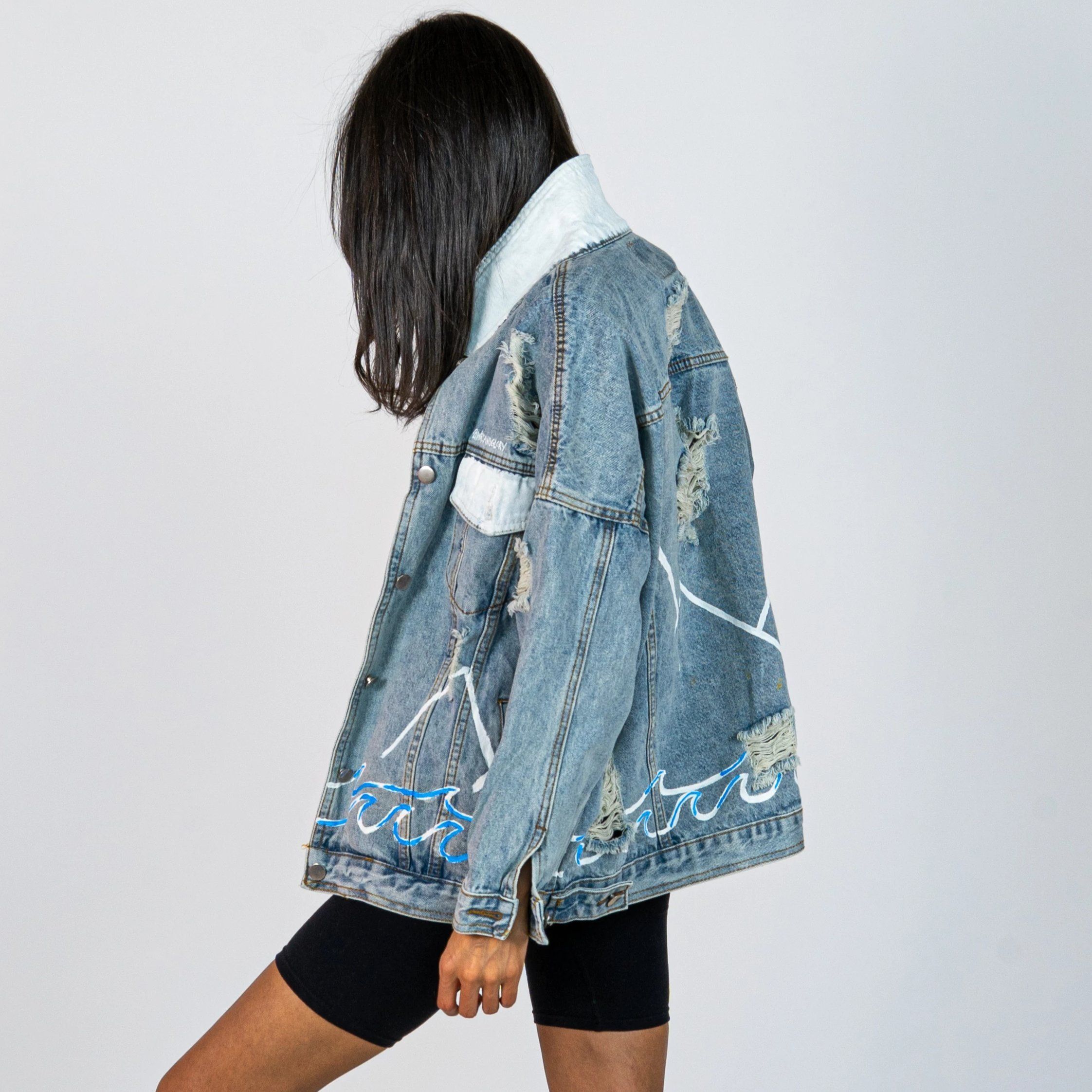 Lighter blue denim wash. Outline of mountain range, ocean waves, and sun setting surrounding entire jacket. Collar and front pockets painted white. Signed @wrenandglory.