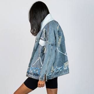 Lighter blue denim wash. Outline of mountain range, ocean waves, and sun setting surrounding entire jacket. Collar and front pockets painted white. Signed @wrenandglory.