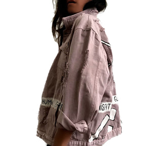 Light blush colored denim. Large eye painted on back, with lines following the shape. A banner spanning the entire jacket painted in white, with black wording. Signed @wrenandglory.