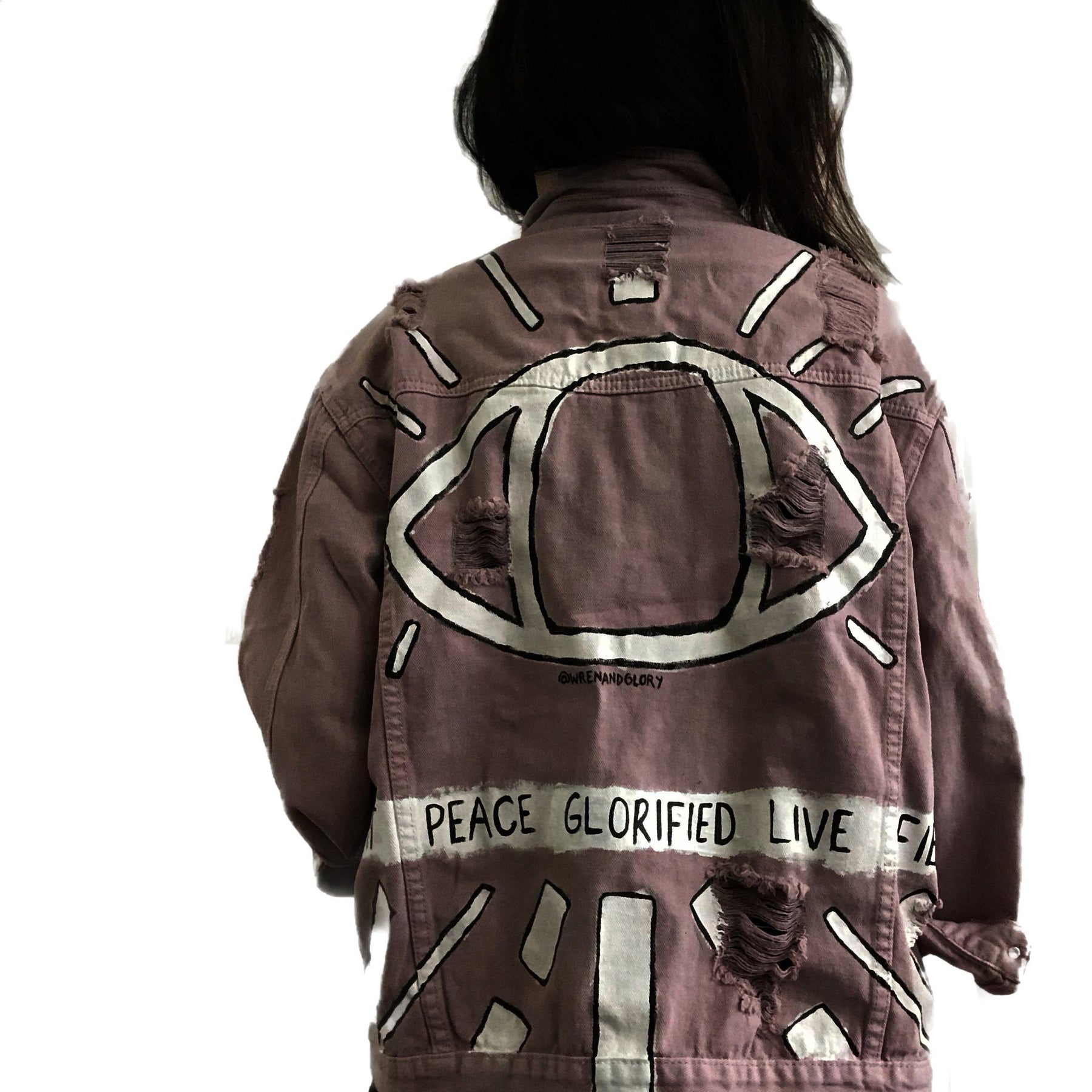 Light blush colored denim. Large eye painted on back, with lines following the shape. A banner spanning the entire jacket painted in white, with black wording. Signed @wrenandglory.