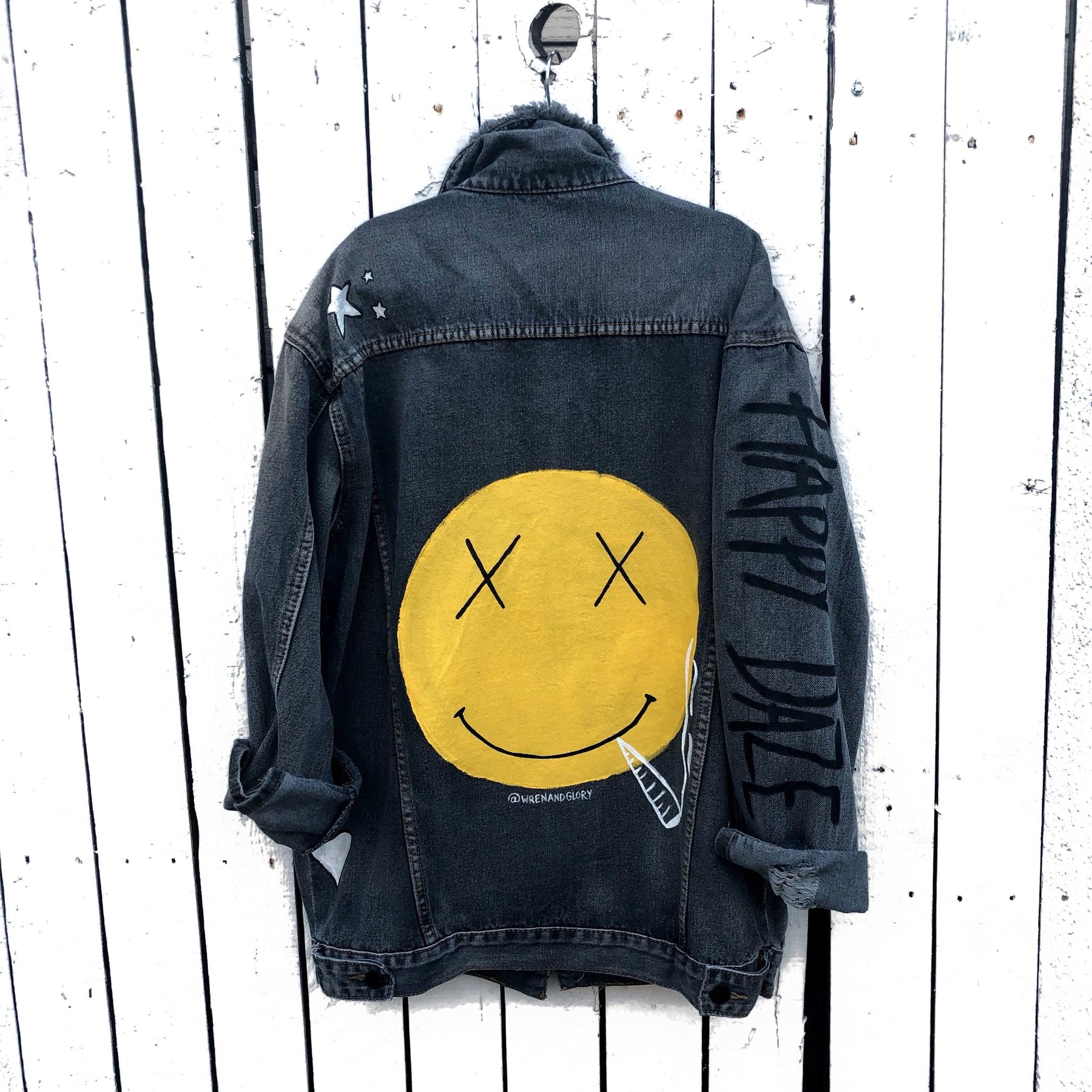 Yellow smiley on faded black denim jacket, with hand painted symbols throughout. Hand painted with white, yellow and black. 'HAPPY DAZE' written down left arm. Signed @wrenandglory