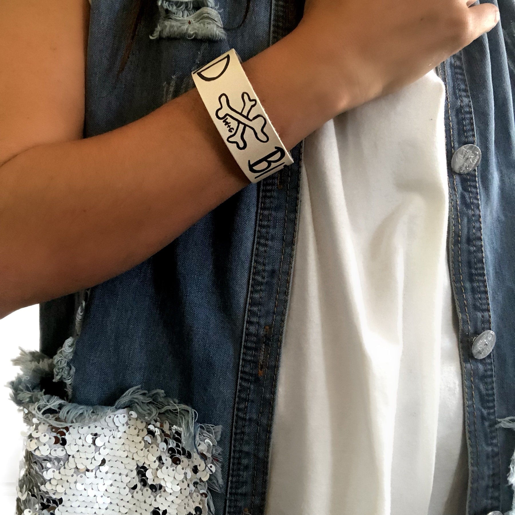 Hand made leather bracelet, hand painted with Bad B*tch and crossbones.  White leather, black paint. Signed W+G