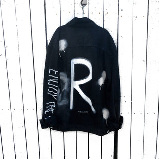Black denim. Initial on back in white, with white and black painted 'splatters' 'Enjoy The Ride' painted in white down the arm Signed @wrenandglory.