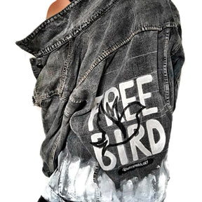 Faded black denim. FREE BIRD painted in white in block letters on back, with a silhouette on a bird in black over it. Signed @wrenandglory.