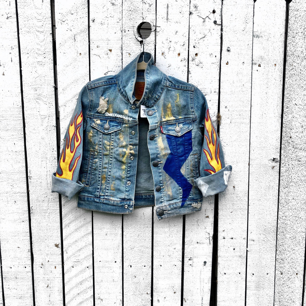 Blue denim jacket. Hand painted design, with stars, flames, and metallics. Childs name available on front, left corner. Each jacket wrapped in a silk wrap bracelet with a child’s charm. Each piece signed @wrenandglory.