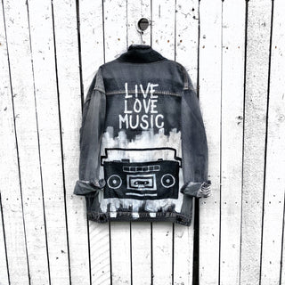 Faded black denim. Boombox painted on back over white base, with wording 'LIVE, LOVE, MUSIC'. Assorted 1 inch pins on front upper side. Signed @wrenandglory.