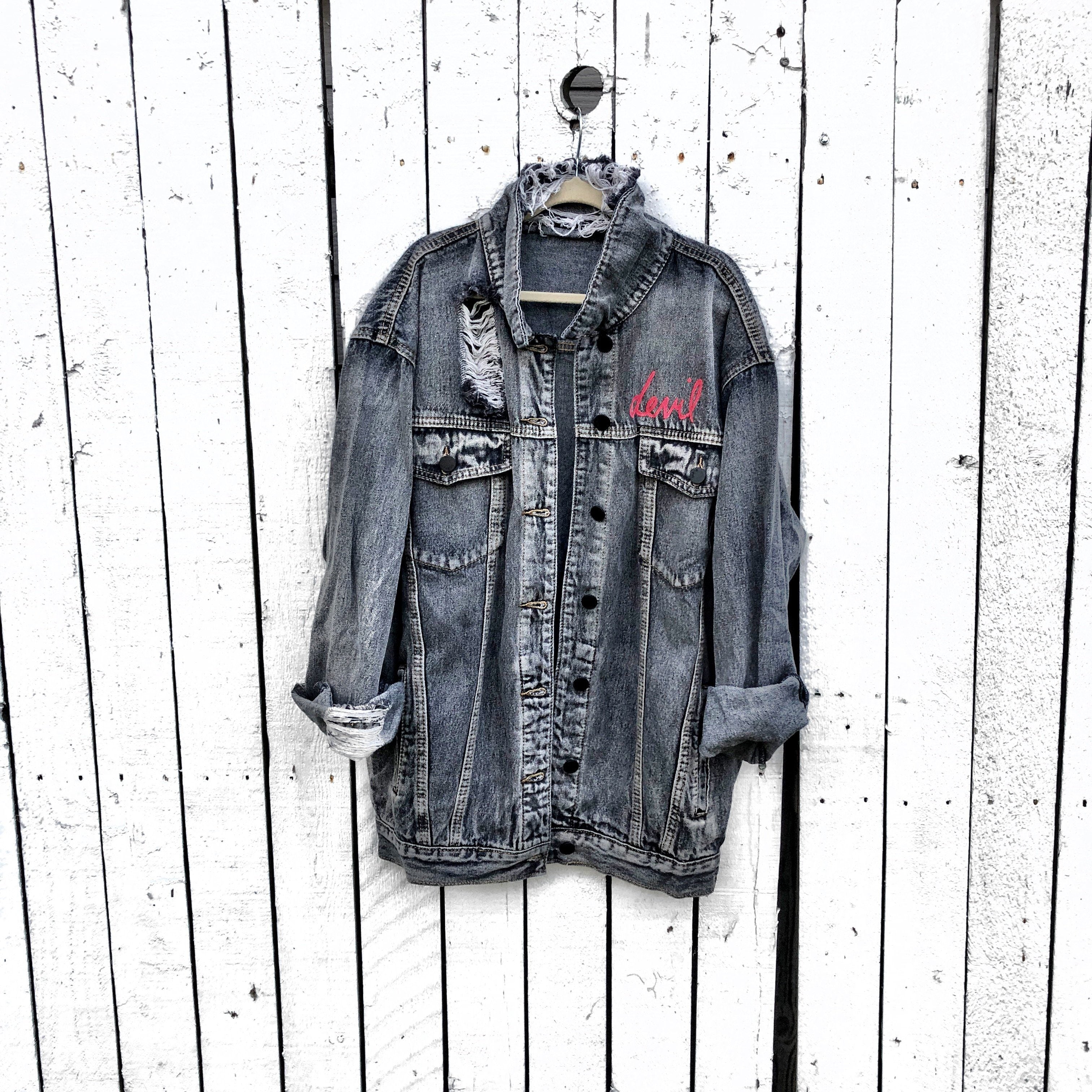 Faded black denim. Red devil wings, horns and tail painted on back, with 'devil' painted in script on front upper corner. Assorted 1 inch pins on front upper side. Signed @wrenandglory.