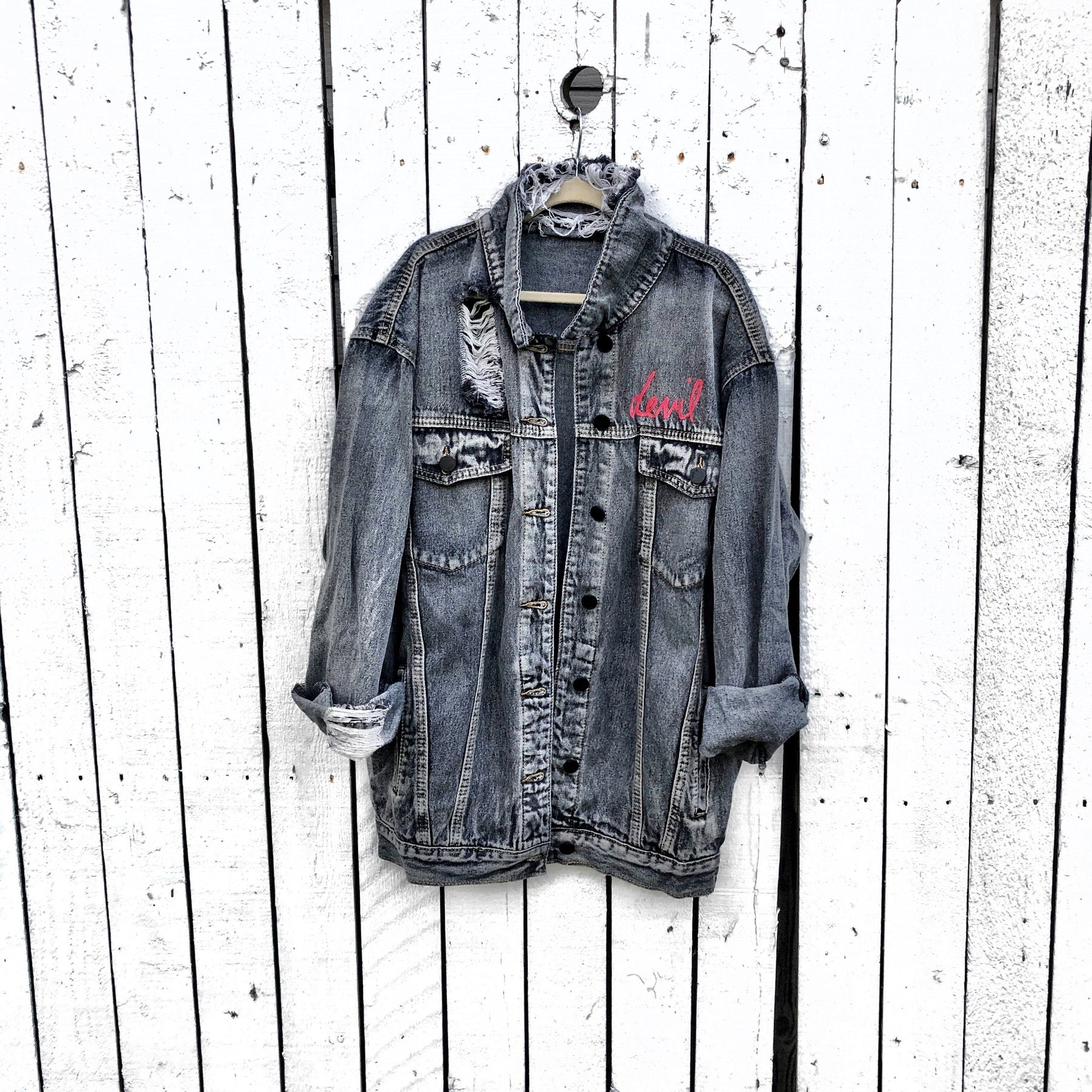 Faded black denim. Red devil wings, horns and tail painted on back, with 'devil' painted in script on front upper corner. Assorted 1 inch pins on front upper side. Signed @wrenandglory.