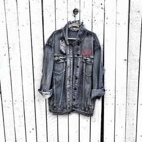 Faded black denim. Red devil wings, horns and tail painted on back, with 'devil' painted in script on front upper corner. Assorted 1 inch pins on front upper side. Signed @wrenandglory.