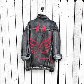 Faded black denim. Red devil wings, horns and tail painted on back, with 'devil' painted in script on front upper corner. Assorted 1 inch pins on front upper side. Signed @wrenandglory.