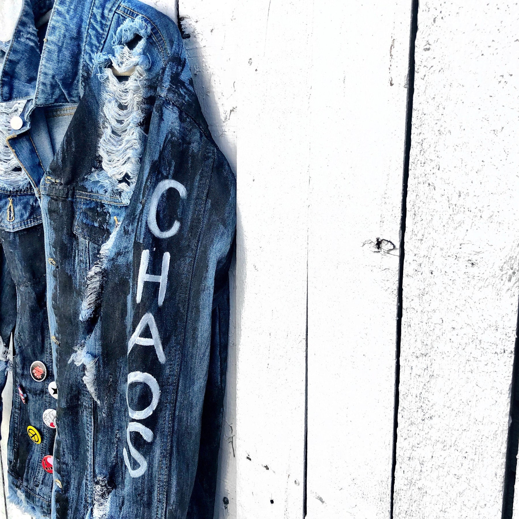Medium blue denim wash. Black base all over, with 'MADE IN NYC' painted on back in white. CHAOS painted down the arm in white. Assorted 1" pins on bottom left, bottom pocket area. Signed @wrenandglory.