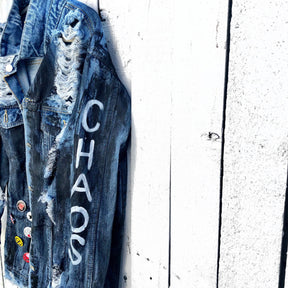 Medium blue denim wash. Black base all over, with 'MADE IN NYC' painted on back in white. CHAOS painted down the arm in white. Assorted 1" pins on bottom left, bottom pocket area. Signed @wrenandglory.