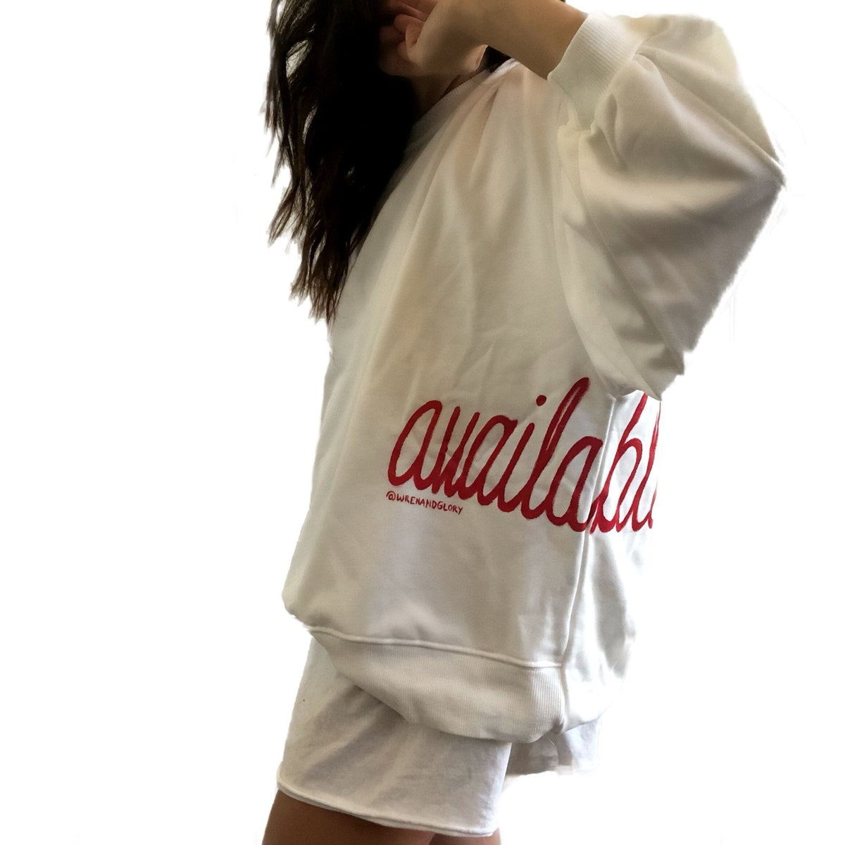 Oversized white sweatshirt. 'Available' painted in script on lower left side, in red. Small red embroidered heart on each lower sleeve. Signed @wrenandglory.