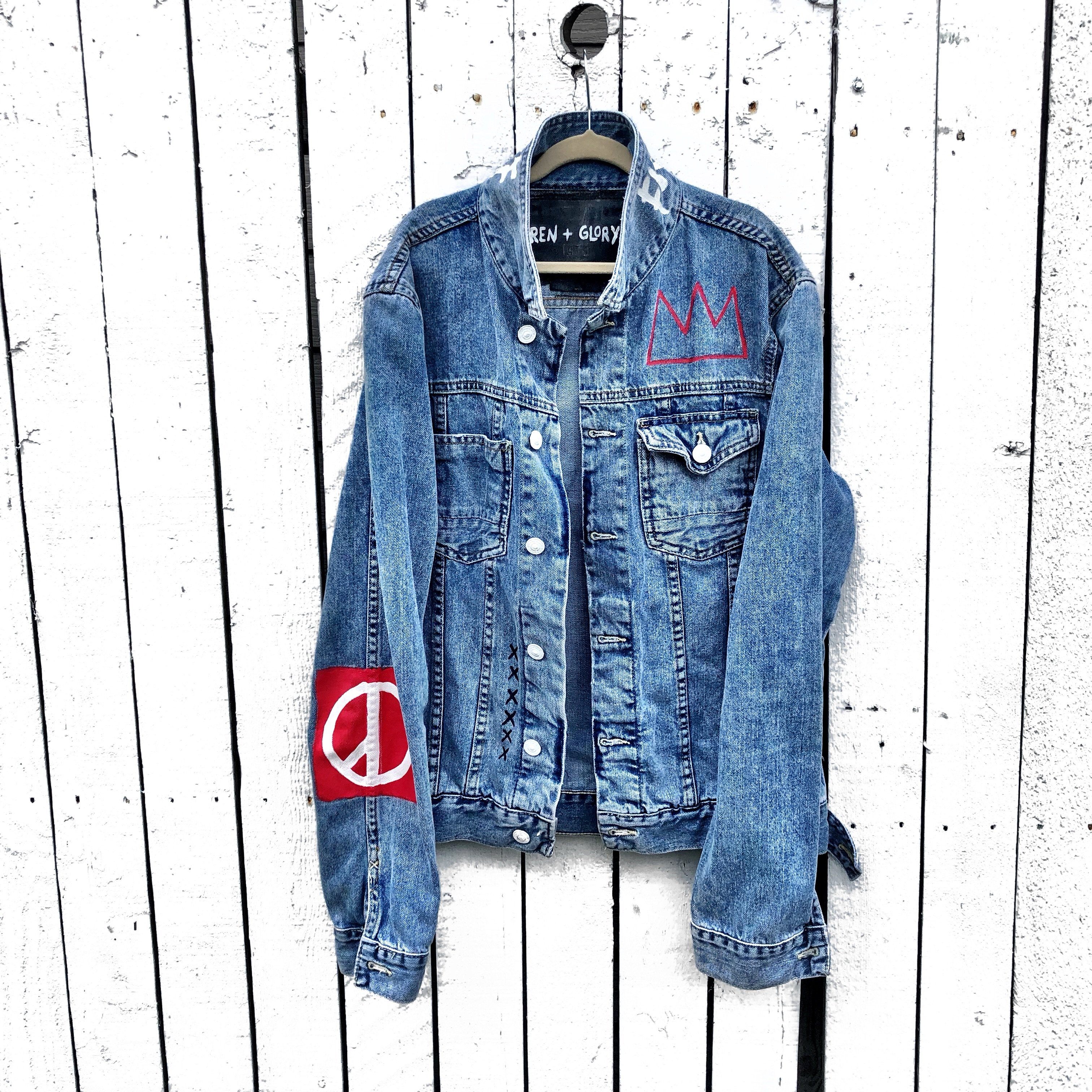 Medium blue denim wash. Black smily with red crown on back. Red crown and design on arm and front. White stripes on lower side on back. 'Fuck Off' painted in white on collar.. Signed @wrenandglory.