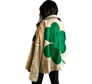 Khaki colored jacket, with green flannel print inside. Large green clover painted on back, with KISS ME down the arm in green and white. Signed @wrenandglory.