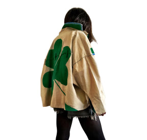 Khaki colored jacket, with green flannel print inside. Large green clover painted on back, with KISS ME down the arm in green and white. Signed @wrenandglory.