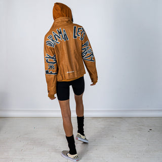 Tan, faux leather jacket with Brown hooded sweatshirt lining the inside and thumbholes at sleeves. 'F*CK DRAMA LET'S PARTY' painted along back of sleeves and upper back of jacket, in black, with white outline. Signed @wrenandglory.