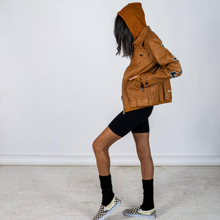 Tan, faux leather jacket with Brown hooded sweatshirt lining the inside and thumbholes at sleeves. 'F*CK DRAMA LET'S PARTY' painted along back of sleeves and upper back of jacket, in black, with white outline. Signed @wrenandglory.
