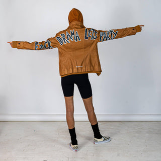 Tan, faux leather jacket with Brown hooded sweatshirt lining the inside and thumbholes at sleeves. 'F*CK DRAMA LET'S PARTY' painted along back of sleeves and upper back of jacket, in black, with white outline. Signed @wrenandglory.