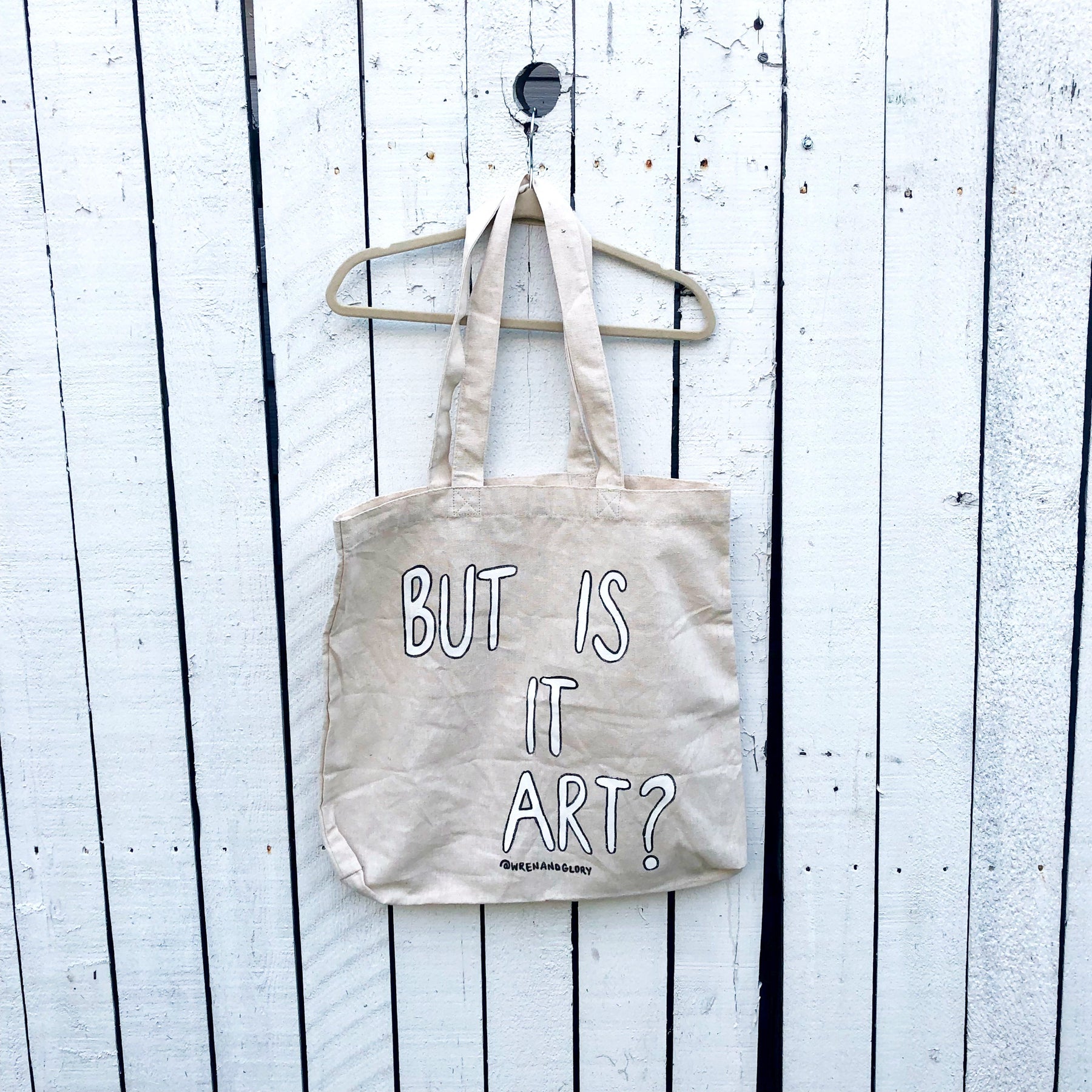 Off white canvas tote bag. Hand painted 'But Is It Art' in white with a black outline. 15.7"x15.7"x3.3 Signed @wrenandglory