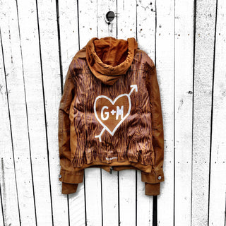 Light brown, faux leather jacket with tan sweatshirt lining the inside, with good and thumbholes at sleeves. Tree trunk painted across entire back in dark brown, with heart carved out and ' ___ + ___' painted inside. Please specify names above. Signed @wrenandglory.