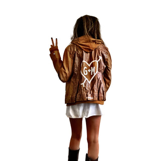 Light brown, faux leather jacket with tan sweatshirt lining the inside, with good and thumbholes at sleeves. Tree trunk painted across entire back in dark brown, with heart carved out and ' ___ + ___' painted inside. Please specify names above. Signed @wrenandglory.