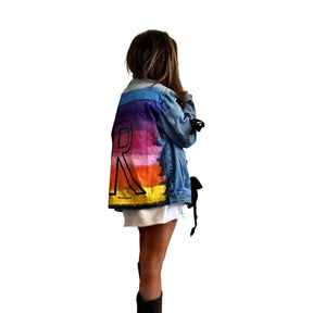 Dark blue denim wash, with velvert ribbon threaded through arms and front, lower left side. Ombre of colored striped on back, with large black initial painted in open block font over the colors. 'BE THE MAGIC' painted on color in black. Please specify initial above. Signed @wrenandglory.