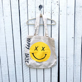 Off white canvas tote bag. Hand painted 'HAPPY DAZE' along the side, with a large yellow smiley in center.